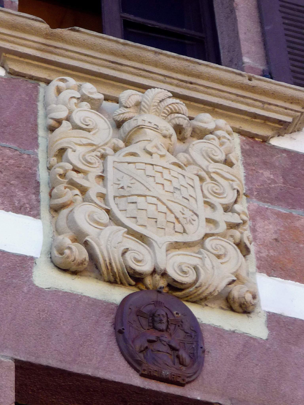 Ein Rathausgebäude mit einem Fenster in der Nähe des Dachs und einem in die Wand gemeißelten Wappen, das detaillierte dekorative Schnitzereien aufweist.