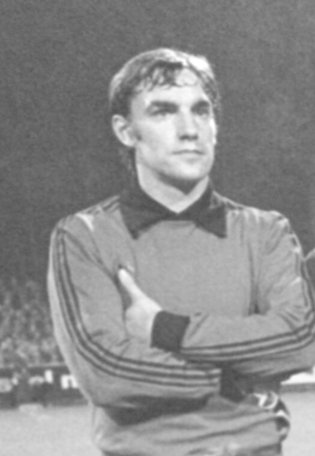 Schwarzes und weißes Foto eines Mannes, der auf einem Fußballfeld steht und die Arme verschränkt hat, umgeben von sitzenden Zuschauern, der als legendärer Torwart von Manchester United gilt, der im Alter von 89 Jahren verstorben ist.