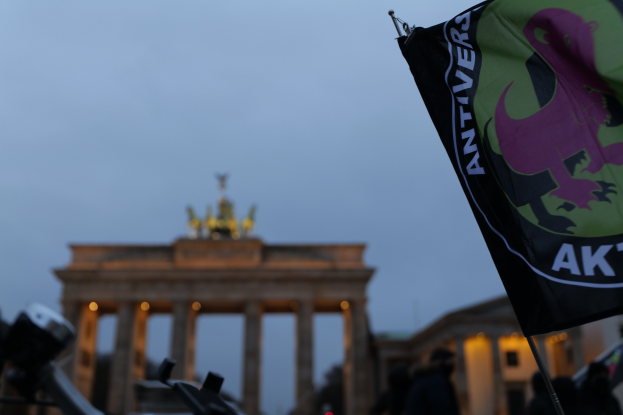 Eine Gruppe von Menschen steht vor dem Reichstagsgebäude in Berlin, Deutschland, mit einer Fahnenstange, die ein Logo und Text trägt, und protestiert gegen die antifaschistische Bewegung.
