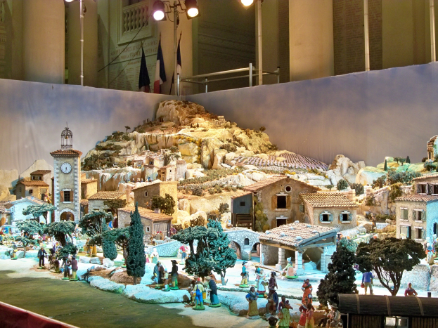 Eine detaillierte Museumsausstellung einer Krippe mit Figuren, Strukturen und natürlichen Elementen, beleuchtet von Museumsbeleuchtung.