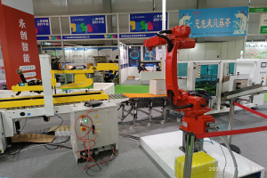 Eine Gruppe von Robotern auf einem Tisch umgeben von Maschinen und Kabeln, mit ein paar Menschen im Hintergrund in einer Fabrikumgebung.