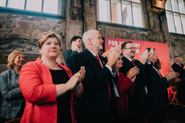 Menschen klatschen feiernd vor einer Menge, mit einem Banner im Hintergrund, das einen Wahlsieg anzeigt.