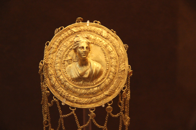 Goldene Medaille mit einer Frauengestalt auf dunklem Hintergrund, mit aufwändiger und luxuriöser Verzierung.