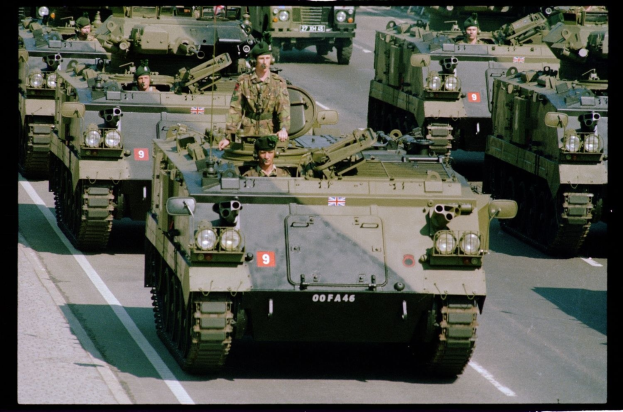 Militärfahrzeuge mit uniformierten Personen auf einer Straße fahrend, mit Text unten.