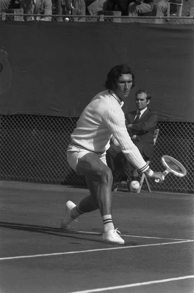 Eine professionelle Tennisspielerin schlägt mit einem Tennisschläger auf einen Ball, während Zuschauer durch ein Maschengitter zuschauen.