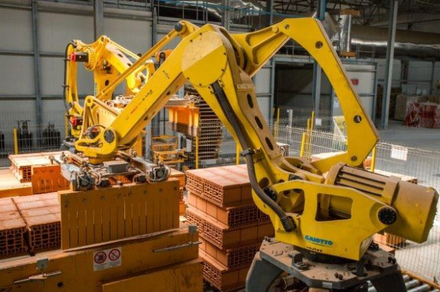 Ein großes Lagerhaus voller numerous boxes, Kräne, ein Zaun, Pfosten und andere Gegenstände, mit einer Wand im Hintergrund, die eine industrielle Umgebung anzeigt.